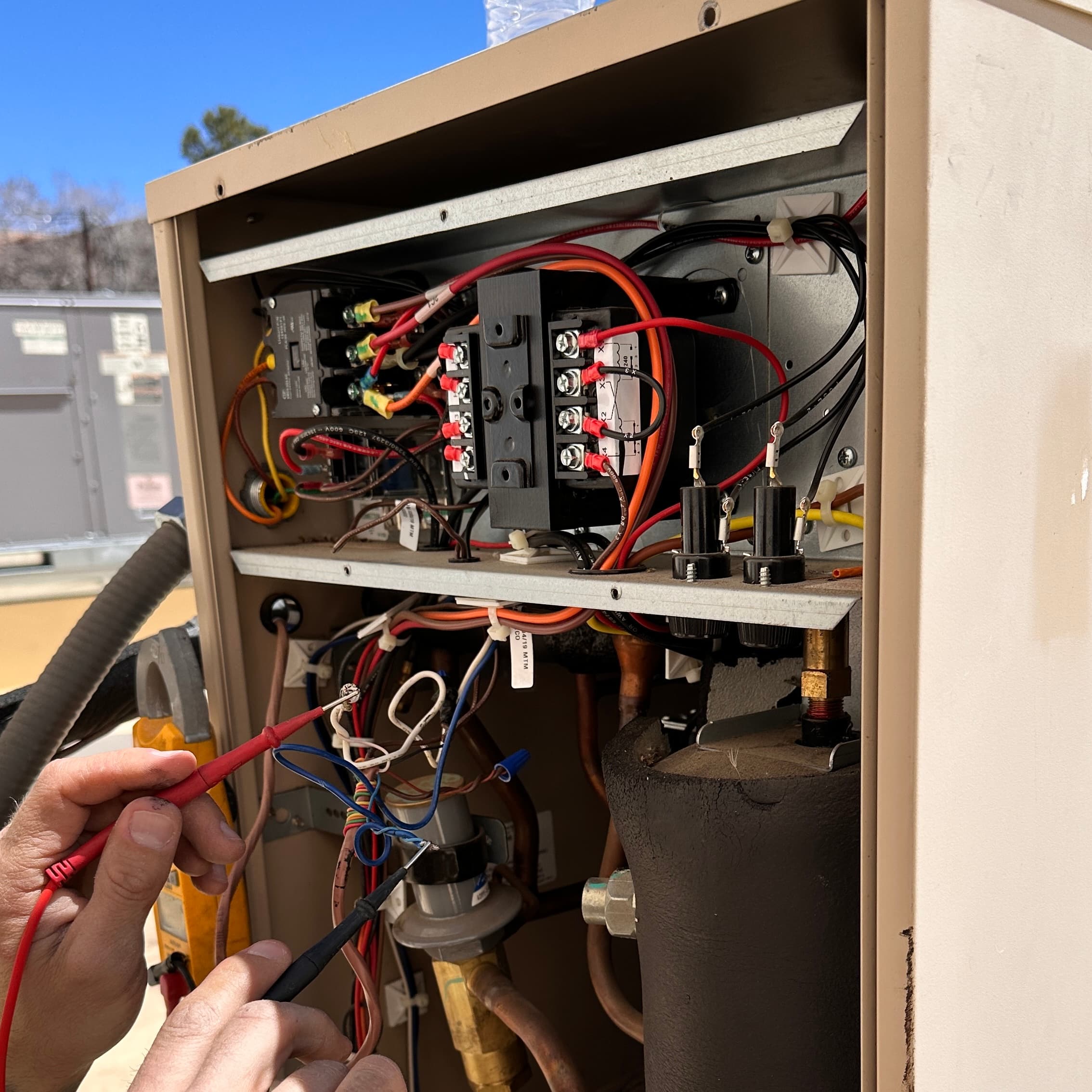 Jello Mechanical HVAC Technician diagnosing an AC electrical panel with a multimeter
